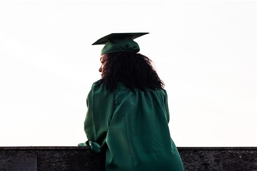 Girl in a green graduation cap and gown leanining on a table looking to her future. 