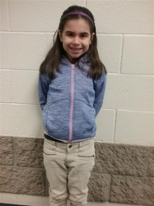 A girl is standing against a white brick wall smiling for a photo. 